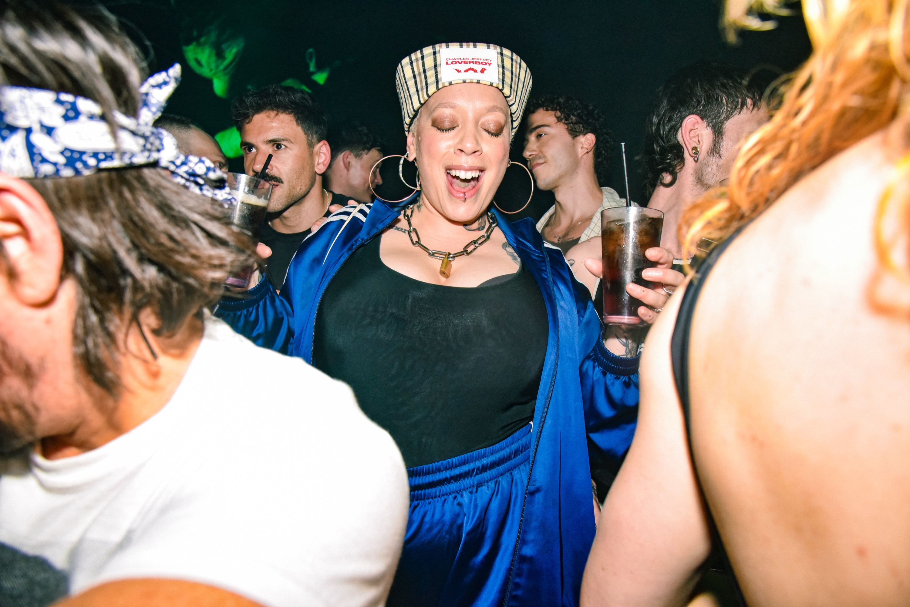 A woman in a blue tracksuit dancing, eyes closed and grinning, in the middle of the crowd